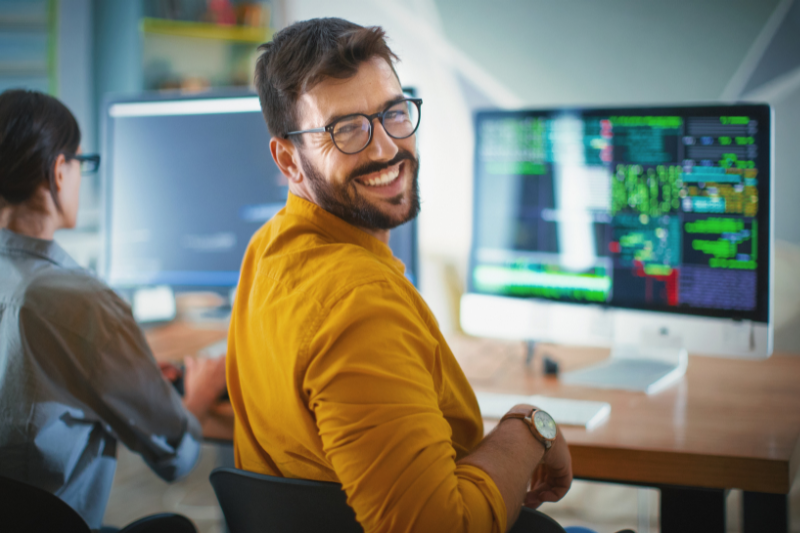Man at a computer in a yellow shirt smiling back at the camera